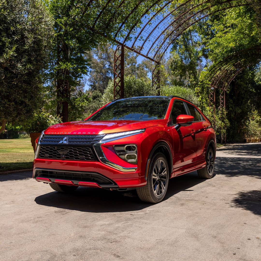 Angled front view of a red 2023 / 2024 Mitsubishi Eclipse Cross Compact SUV parked under an archway in a park