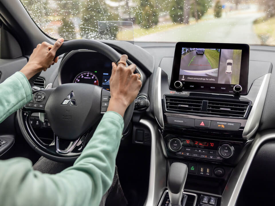 Hands on the steering wheel of a 2023 / 2024 Mitsubishi Eclipse Cross Compact SUV. The screen shows the Multi-View Camera System. 