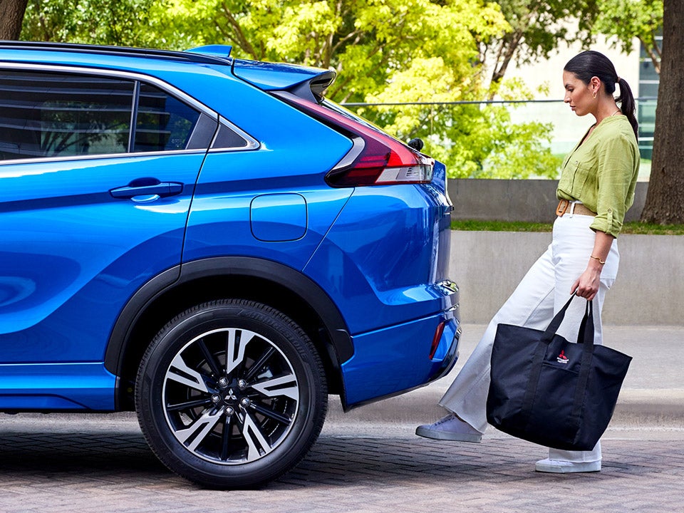 Side view of the back of a blue 2023 / 2024 Mitsubishi Eclipse Cross Compact SUV. A person has their foot under the kick motion sensor to automatically open the trunk