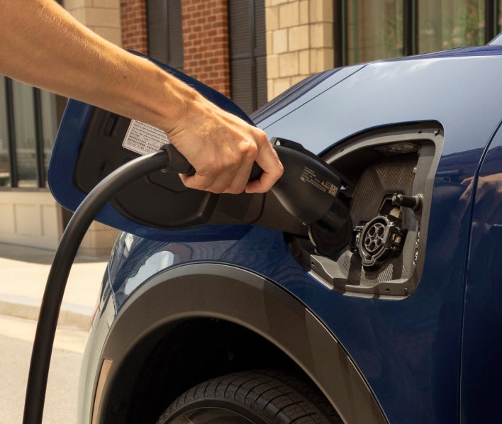 A man standing at the side of his blue 2027 Mitsubishi Eclipse Sportback EV and charging it.