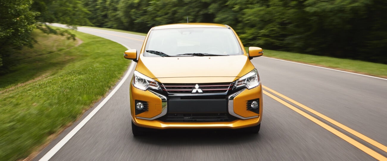 Front view of a sand yellow metallic 2022 & 2023 Mitsubishi Mirage driving fast on the road