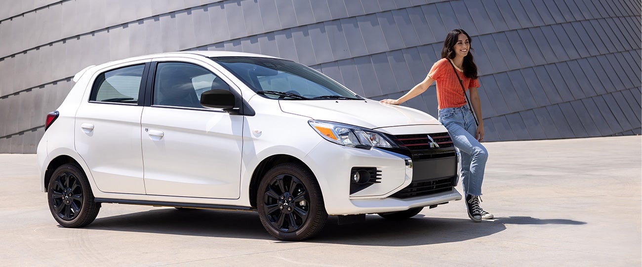 Woman leaning on a parked white 2023 Mitsubishi Mirage hatchback