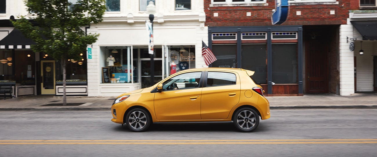 A yellow 2023 Mitsubishi Mirage hatchback driving on a city road