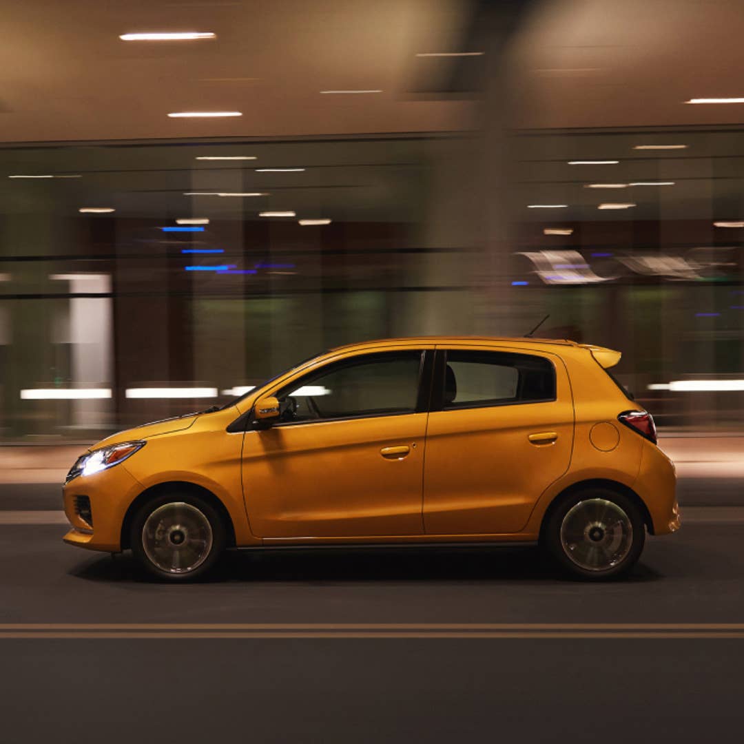 Side view of a yellow 2023 Mitsubishi Mirage hatchback driving fast in the city at night