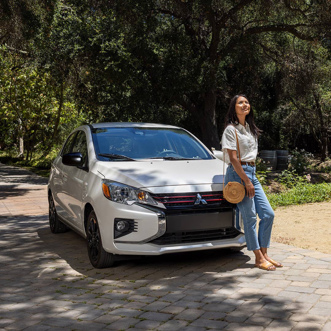 Woman leaning on a parked white 2023 Mitsubishi Mirage hatchback