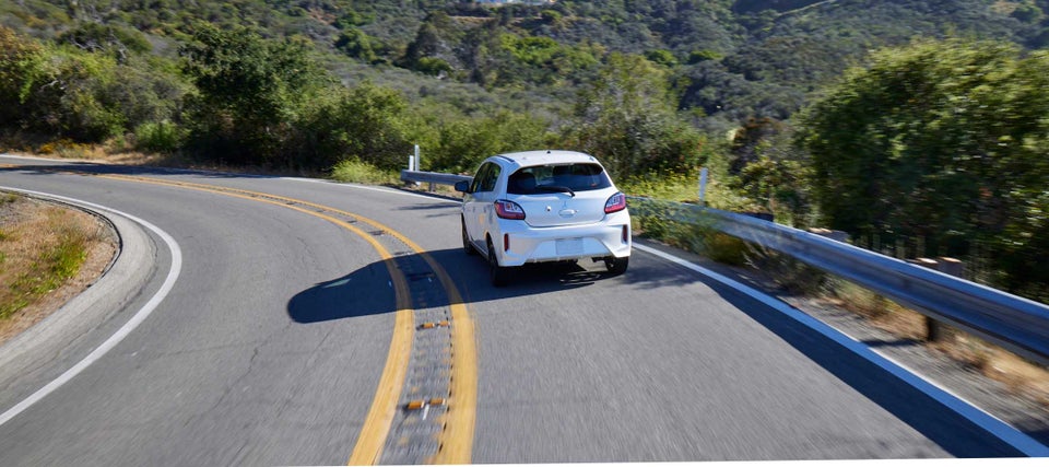 A white Mitsubishi Mirage driving away on a road.