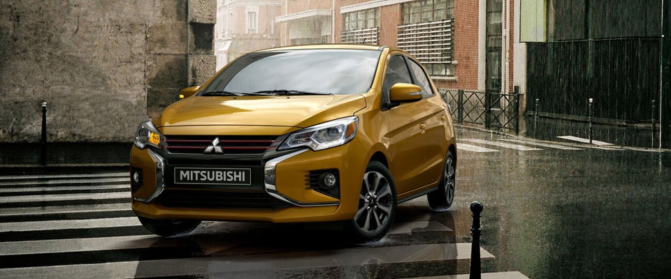A yellow Mitsubishi Mirage parked in the rain.