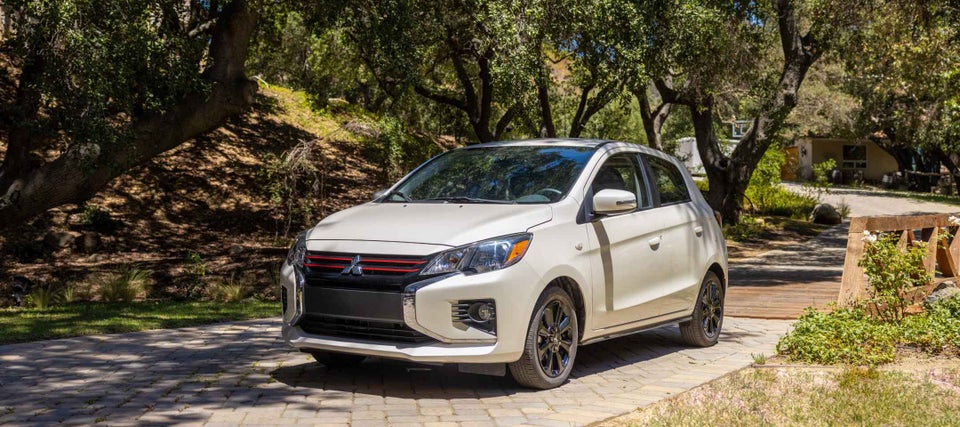 A white 2024 Mitsubishi Mirage Compact Hatchback parked in a forested park