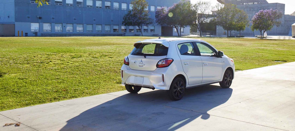 A white Mitsubishi Mirage parked next to buildings.