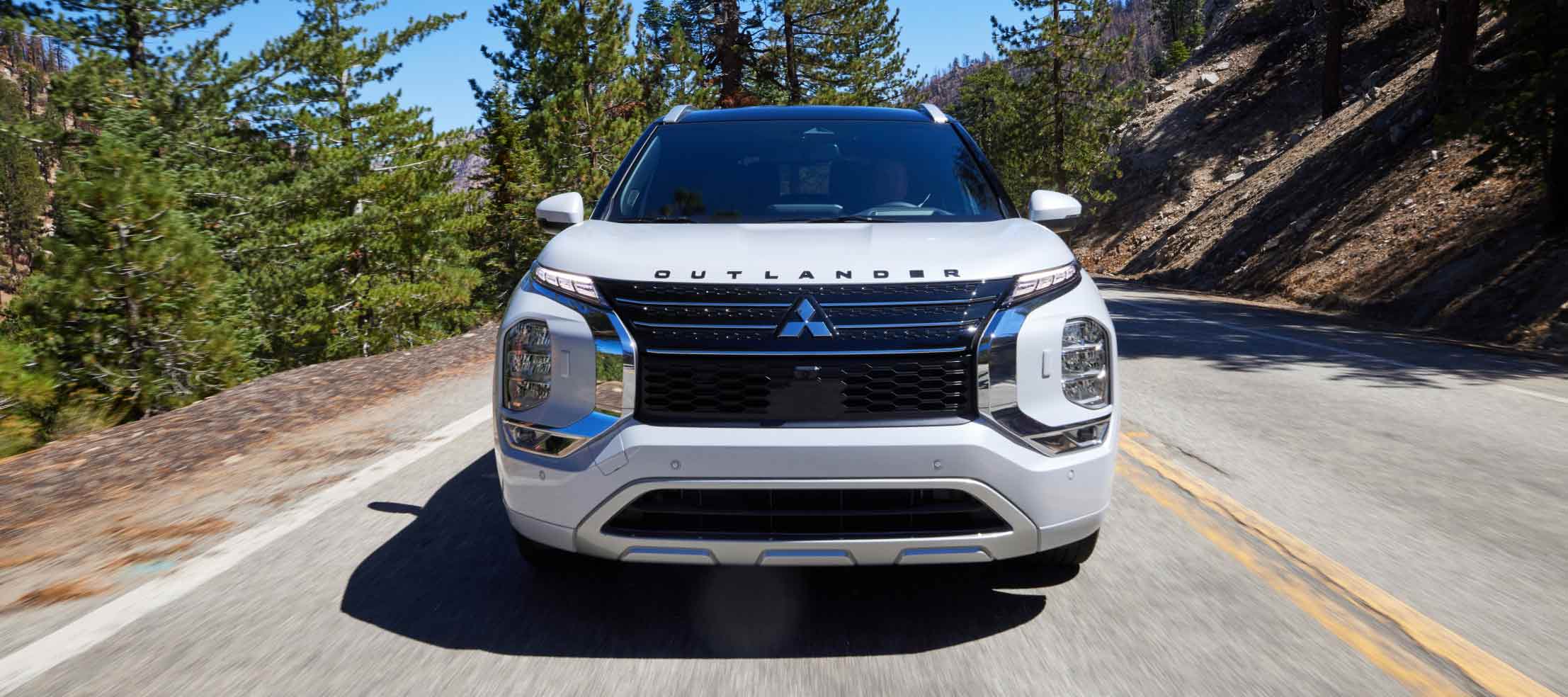 Front view of a white 2023 Mitsubishi Outlander PHEV SUV driving on a mountain road