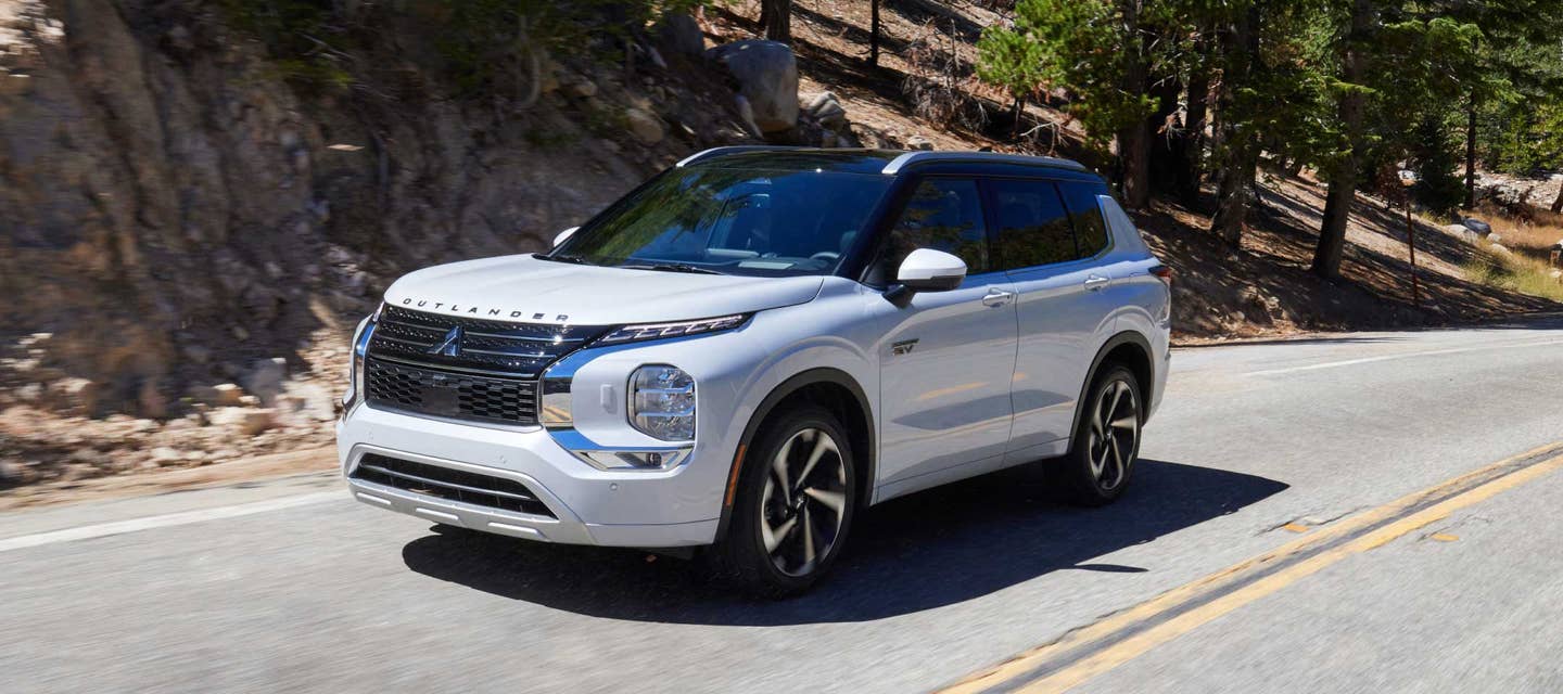 Angled view of a white 2024 / 2025 Mitsubishi Outlander PHEV SUV driving on the road