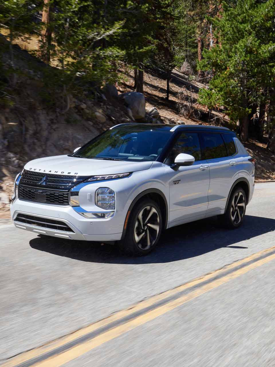 Angled view of a white 2024 / 2025 Mitsubishi Outlander PHEV SUV driving on the road