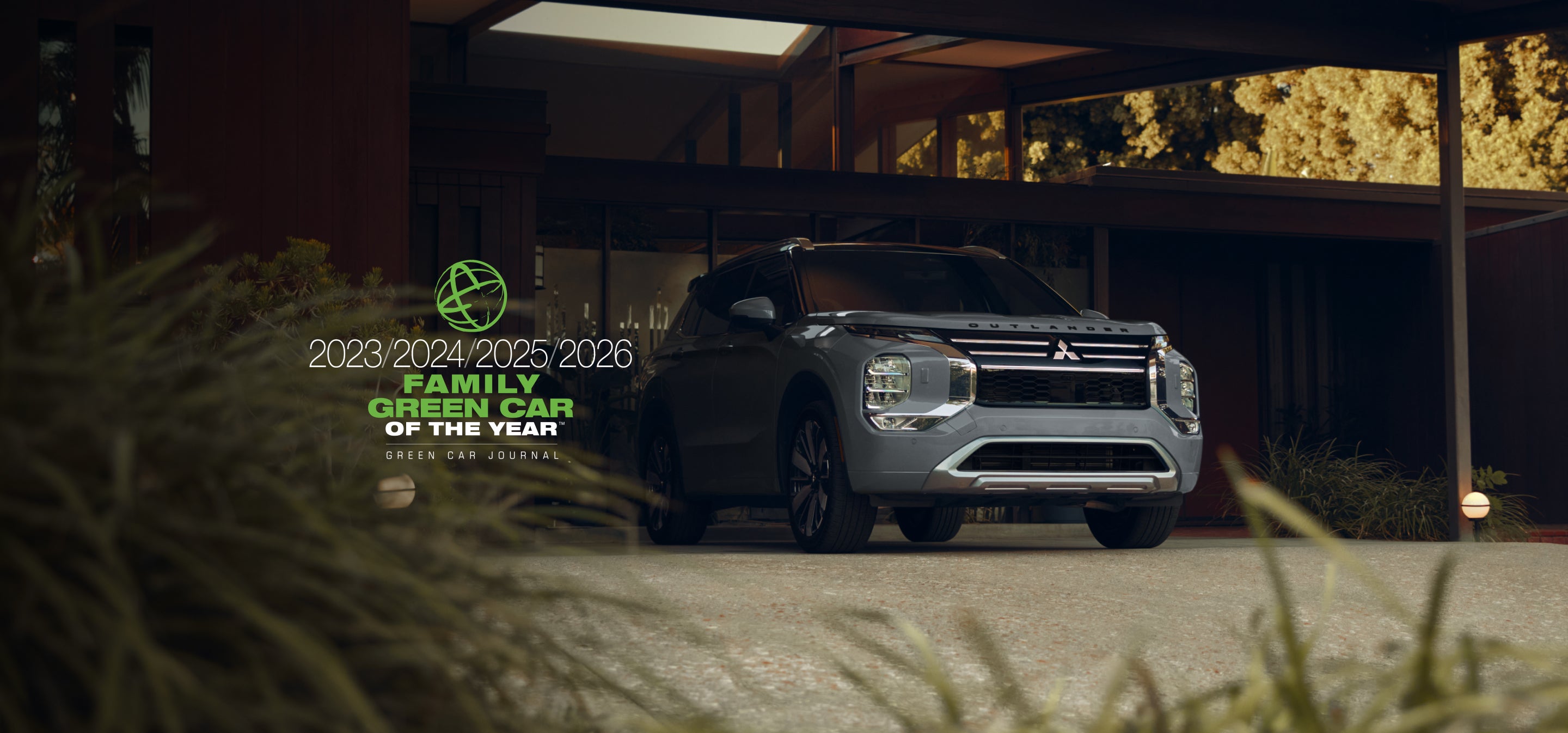 2026 Mitsubishi Outlander PHEV parked in front of a building with a text overlay that says 2025 Family Green Car of the Year from Green Car Journal