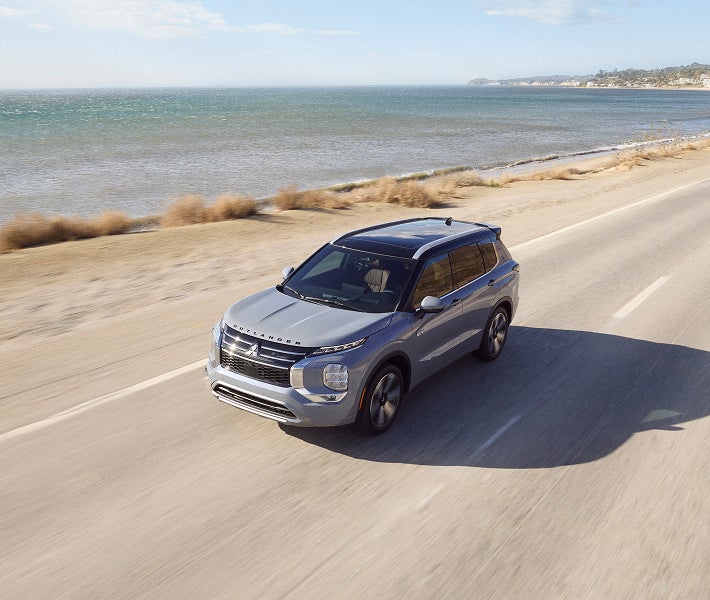 2026 Mitsubishi Outlander PHEV SUV driving on a road beside an ocean