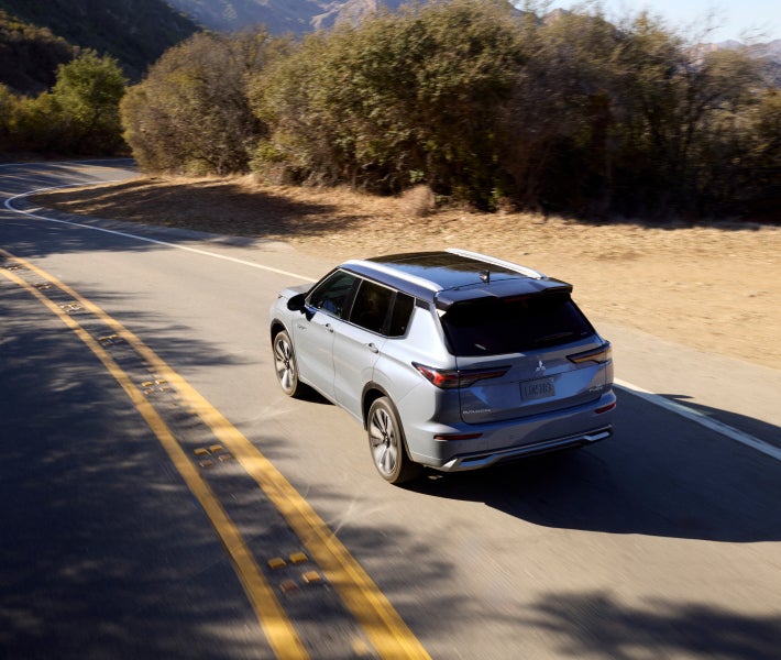 Angled view from above and behind a 2026 Mitsubishi Outlander PHEV SUV driving on a highway demonstrating Speed Limit Assist