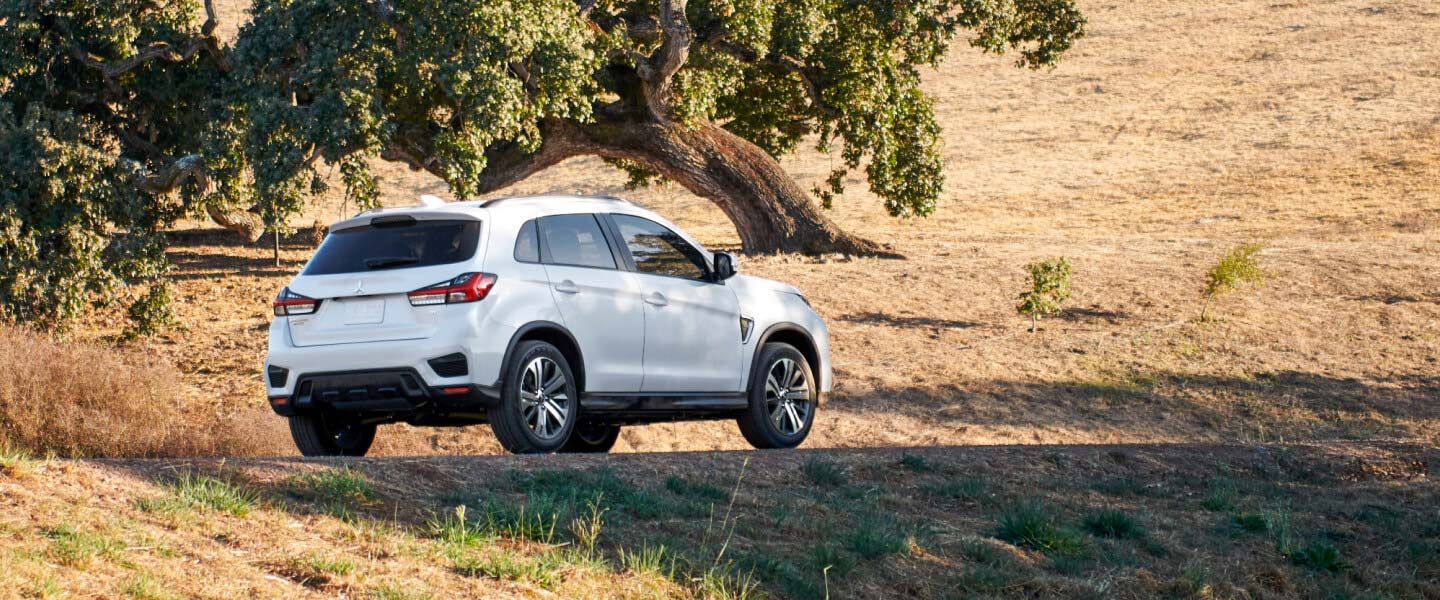 Rear and side view of a white 2022 Mitsubishi Outlander Sport driving in a rural road