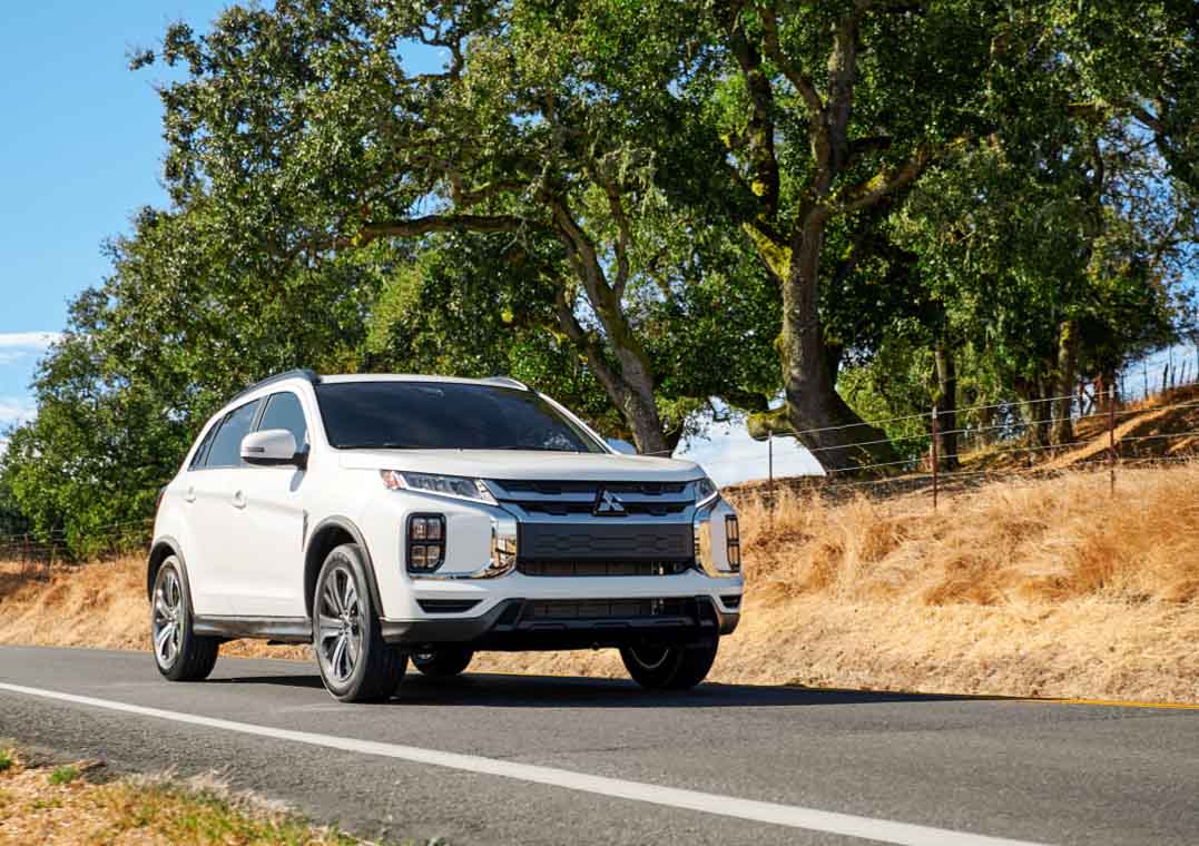 Angled view of a white 2023 Mitsubishi Outlander Sport SUV driving on a road
