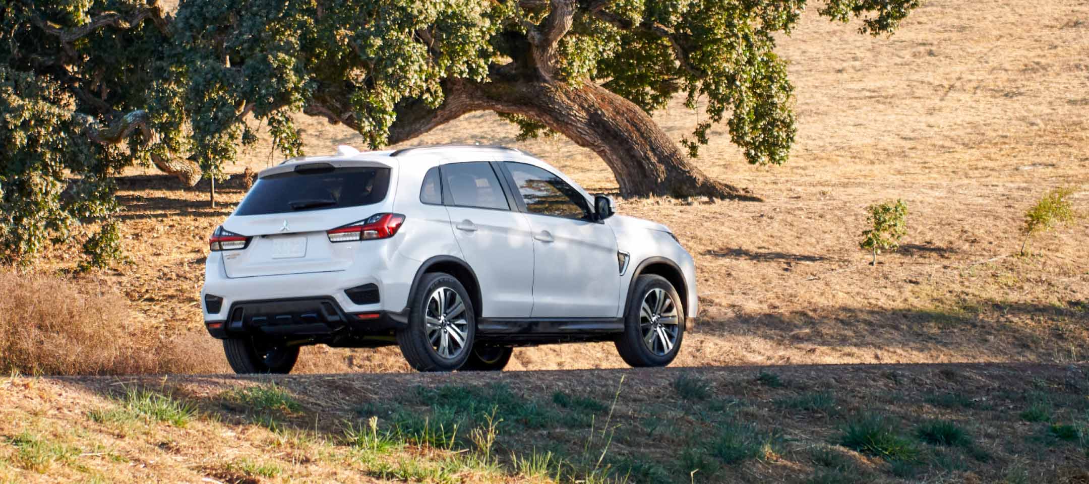 Back and side view of a white 2023 Mitsubishi Outlander Sport SUV driving off-road