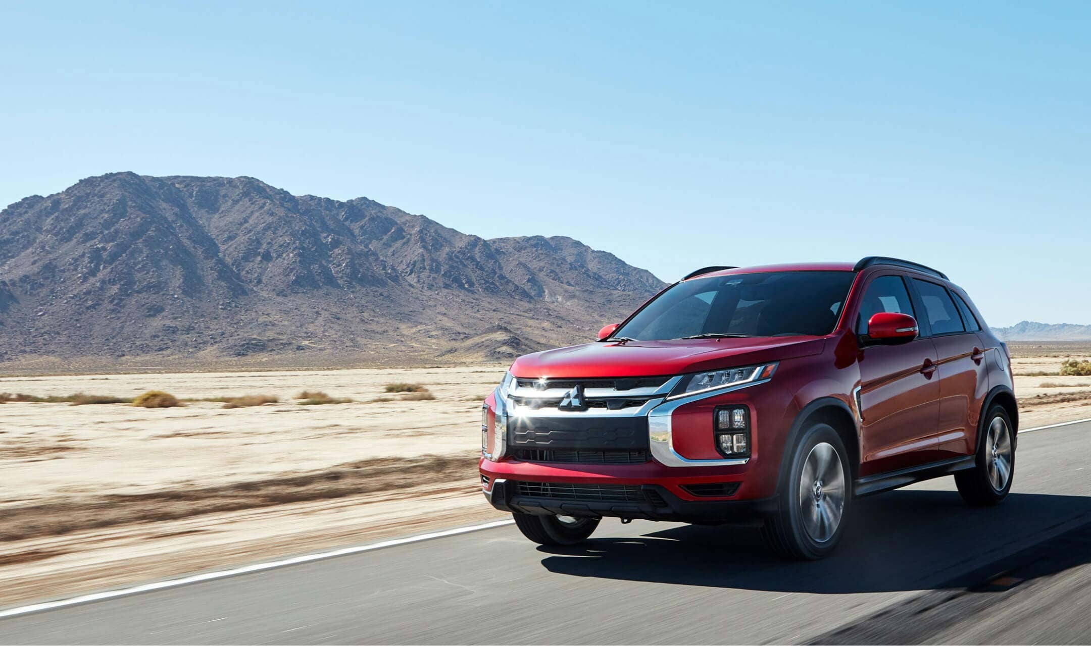 Angled view of a red 2023 Mitsubishi Outlander Sport SUV driving in the desert