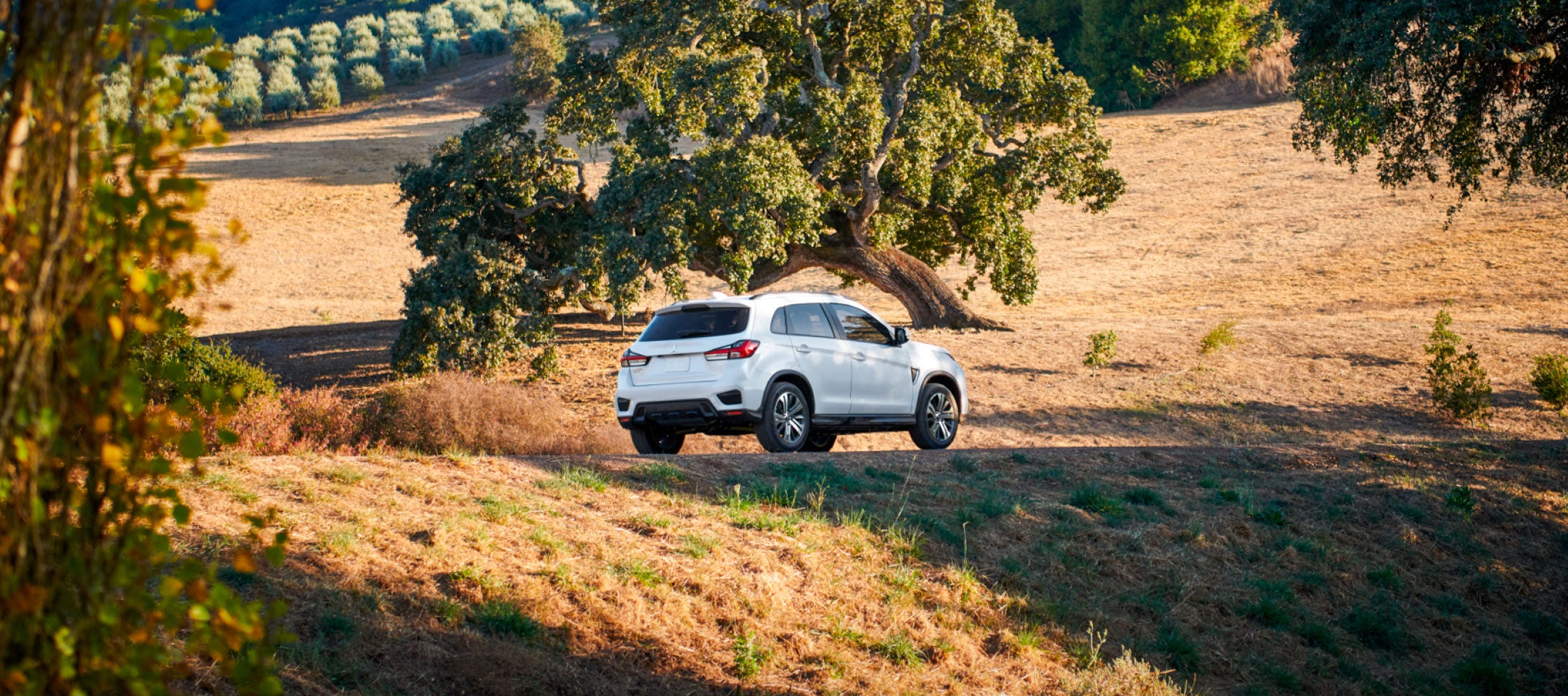 Angled back view of a white 2024 Mitsubishi Outlander Sport SUV driving on a hill