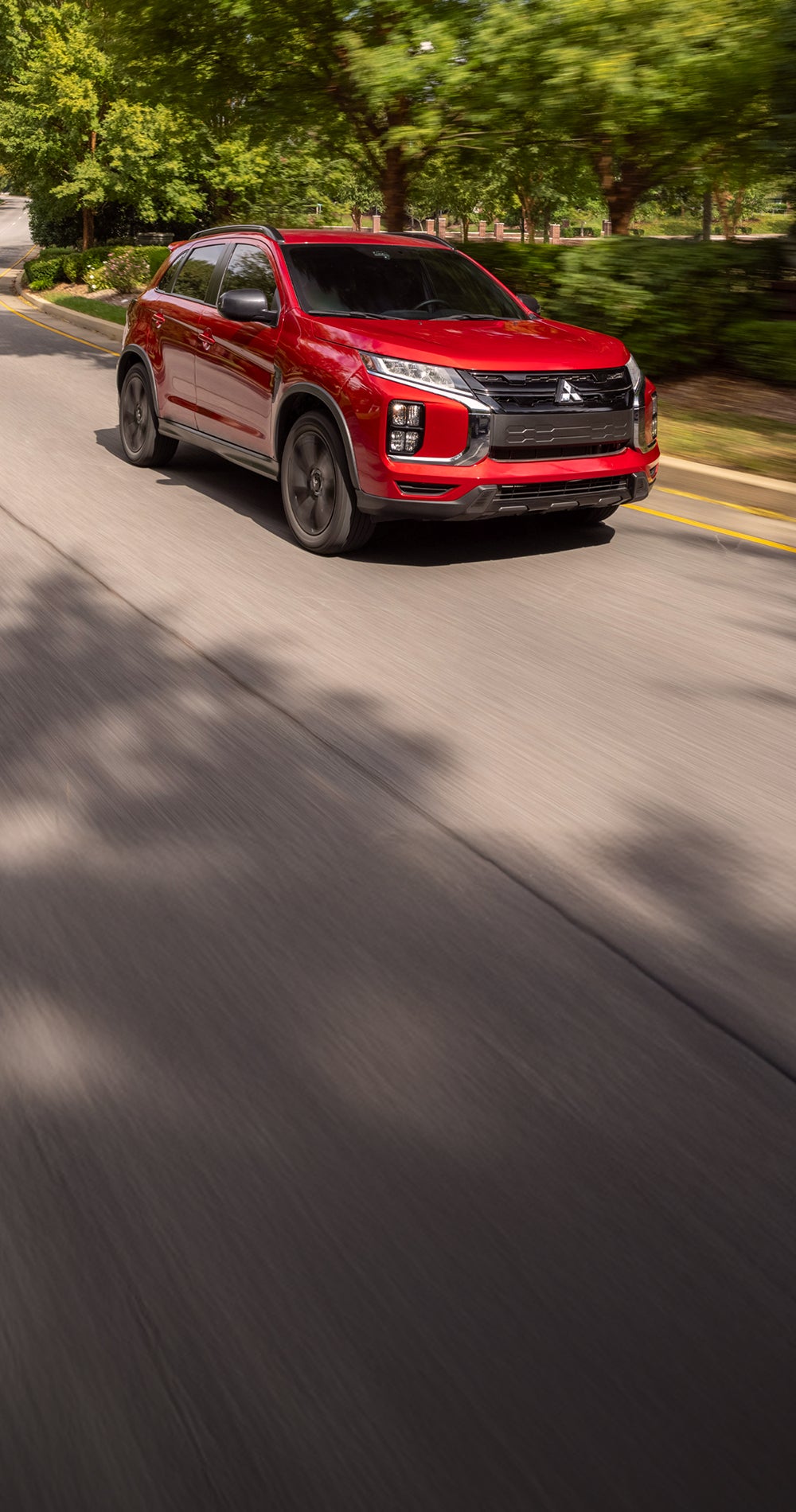 Red 2026 Mitsubishi Outlander Sport SUV driving on a road lined with trees