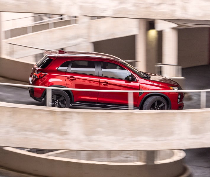 Side profile of red 2026 Mitsubishi Outlander Sport SUV partially obscured by a railing 