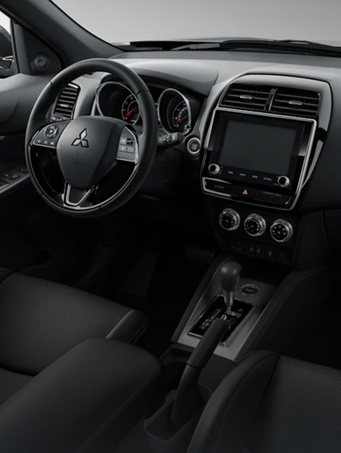 View from the rear seats of the drivers seat, steering wheel, dashboard, and climate controls in the 2027 Mitsubishi Outlander Sport