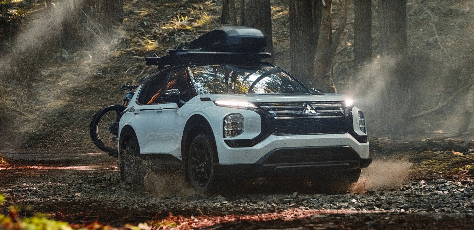 White Mitsubishi Outlander Trail Edition driving through a wooded forest.