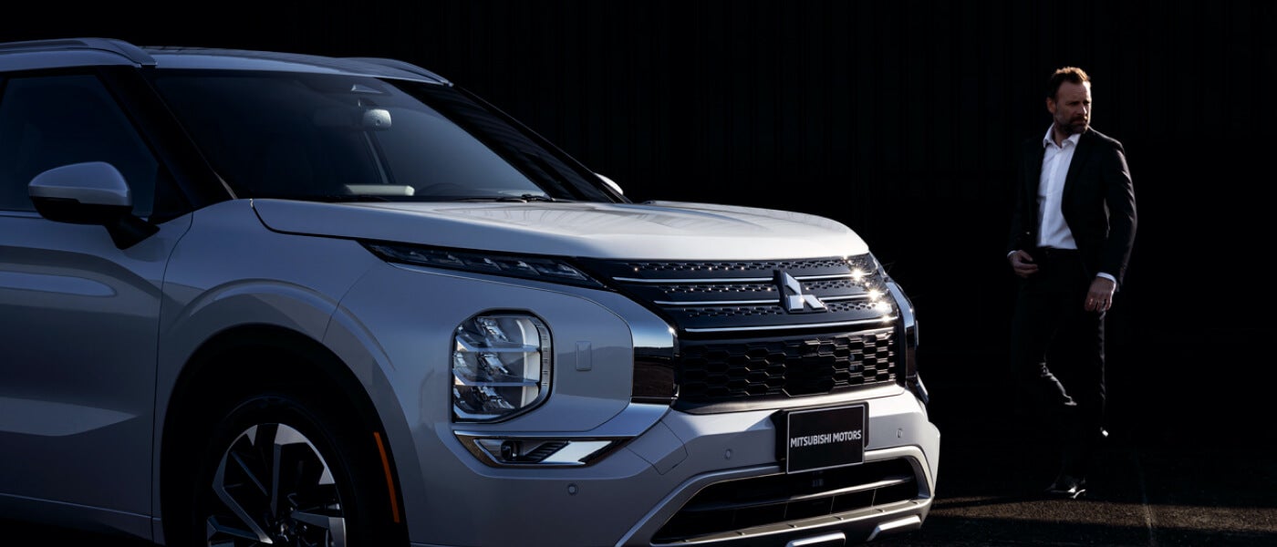 Man walking towards a parked white 2022 Mitsubishi Outlander SUV