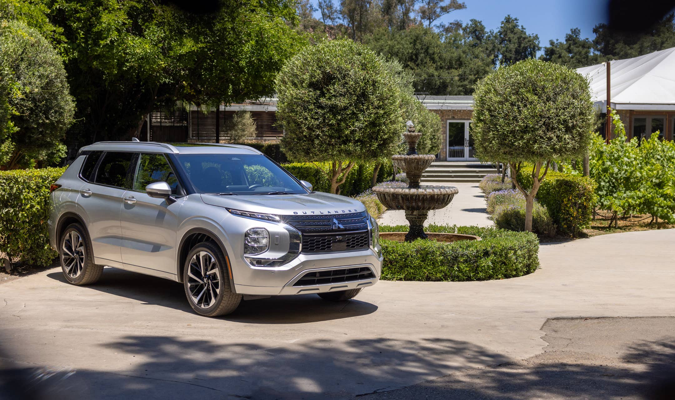 Front and side view of a silver 2023 Mitsubishi Outlander SUV parked in a garden