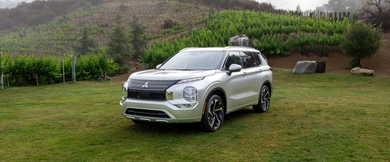 Angled view of a silver 2023 Mitsubishi Outlander SUV parked in a green field