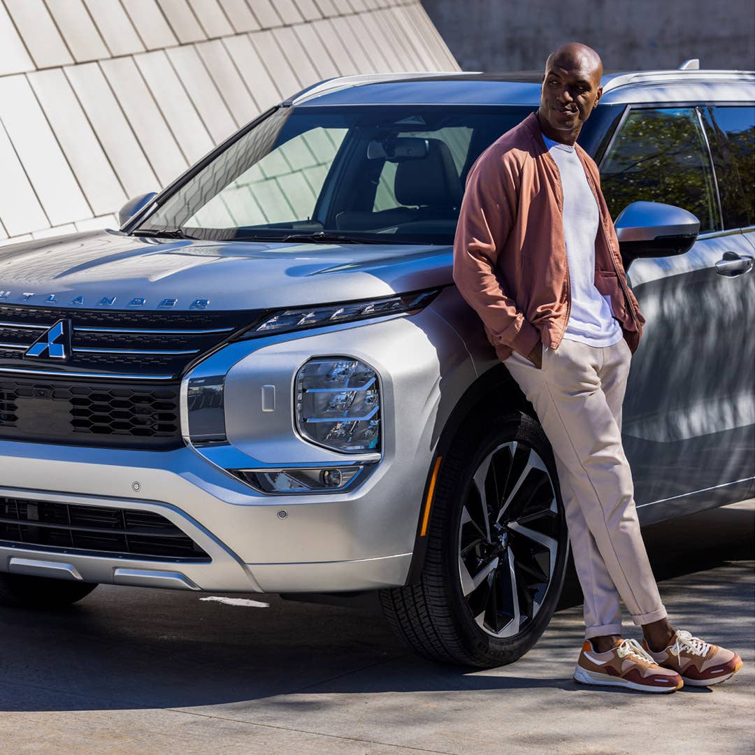 A man leaning on a silver 2023 Mitsubishi Outlander SUV