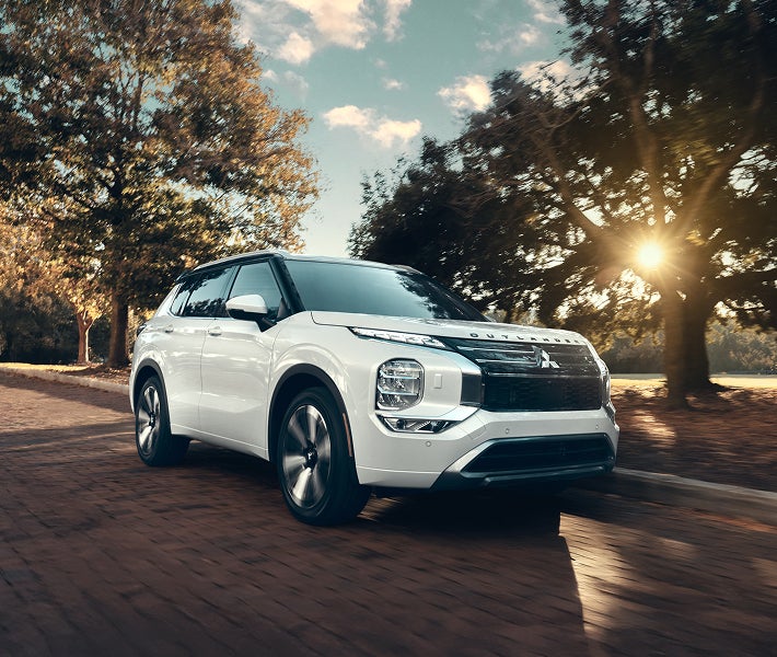 2026 Mitsubishi Outlander SUV driving on a road lined with trees showing off the Speed Limit Assist feature