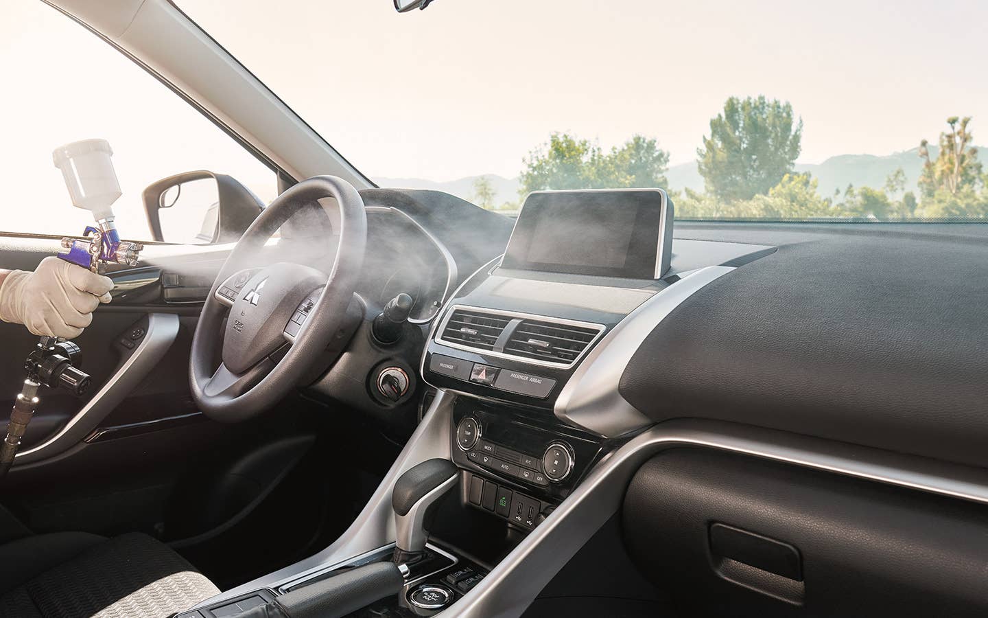 A Mitsubishi technician spraying Diamond Premium Care car disinfectant and deodorizer into the interior of a vehicle.
