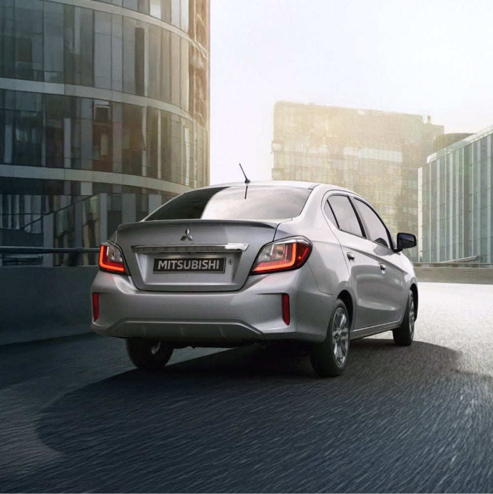 A silver Mitsubishi Mirage G4 seen from behind, parked in front of glass buildings. 