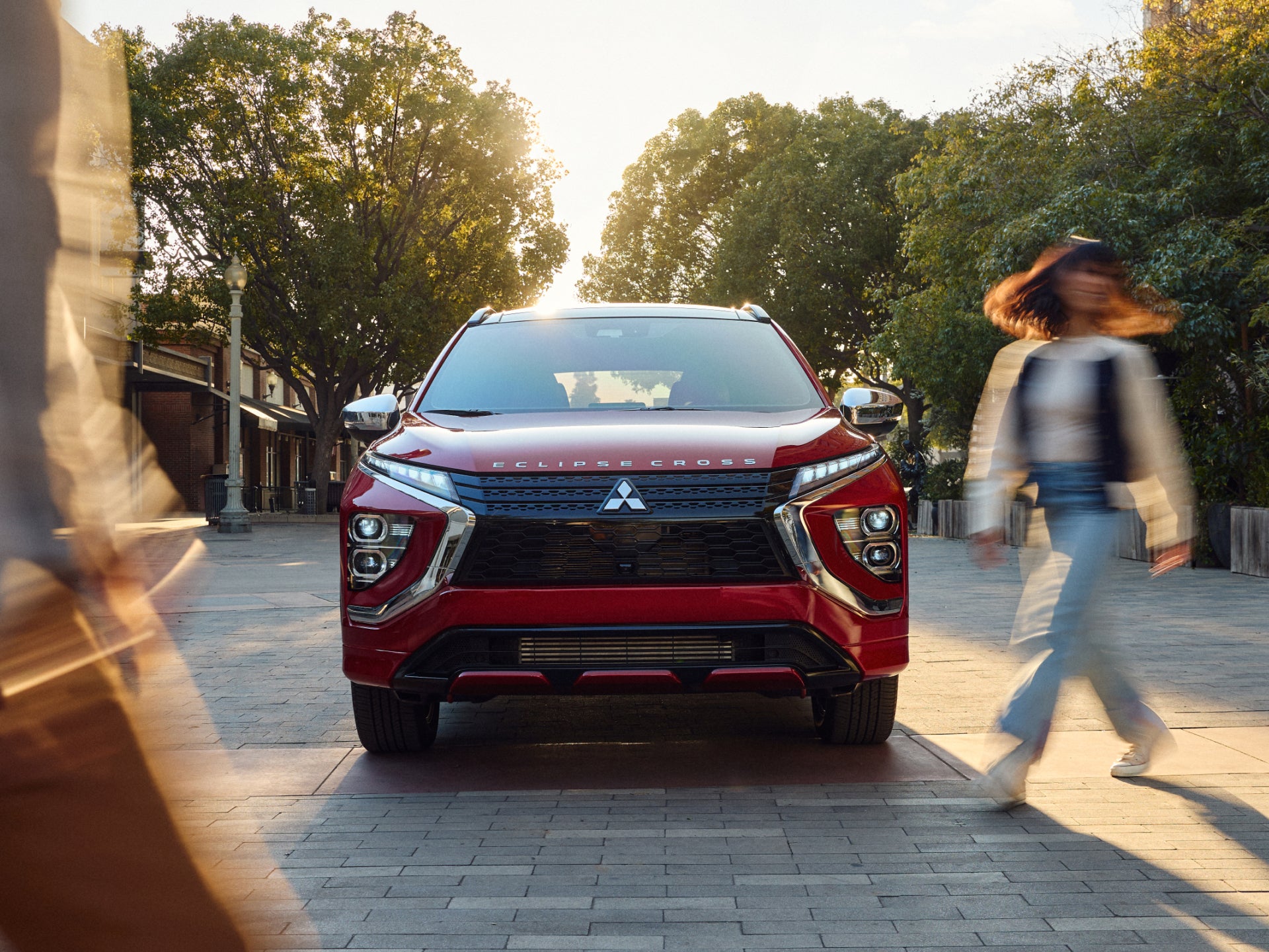 Blurry figure walking beside a red Mitsubishi Eclipse Cross compact crossover SUV.
