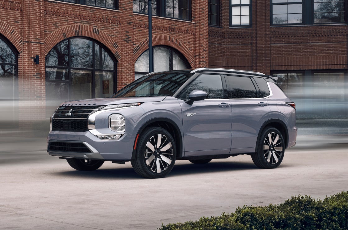Moonstone Mitsubishi Outlander PHEV driving in front of a brick buildling.